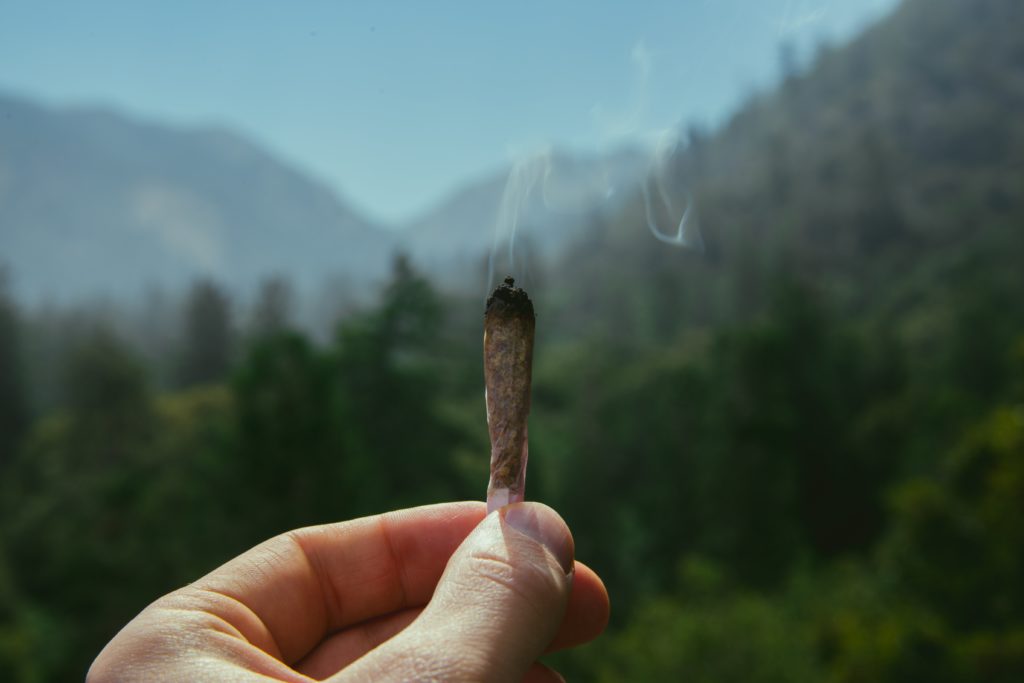 Ukraine and Cannabis - a hand holding out a joint against a mountain landscape background