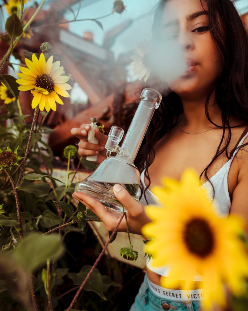 Have yourself a happy little 4/20 - a woman hits a glass bong, surrounded by sunflowers